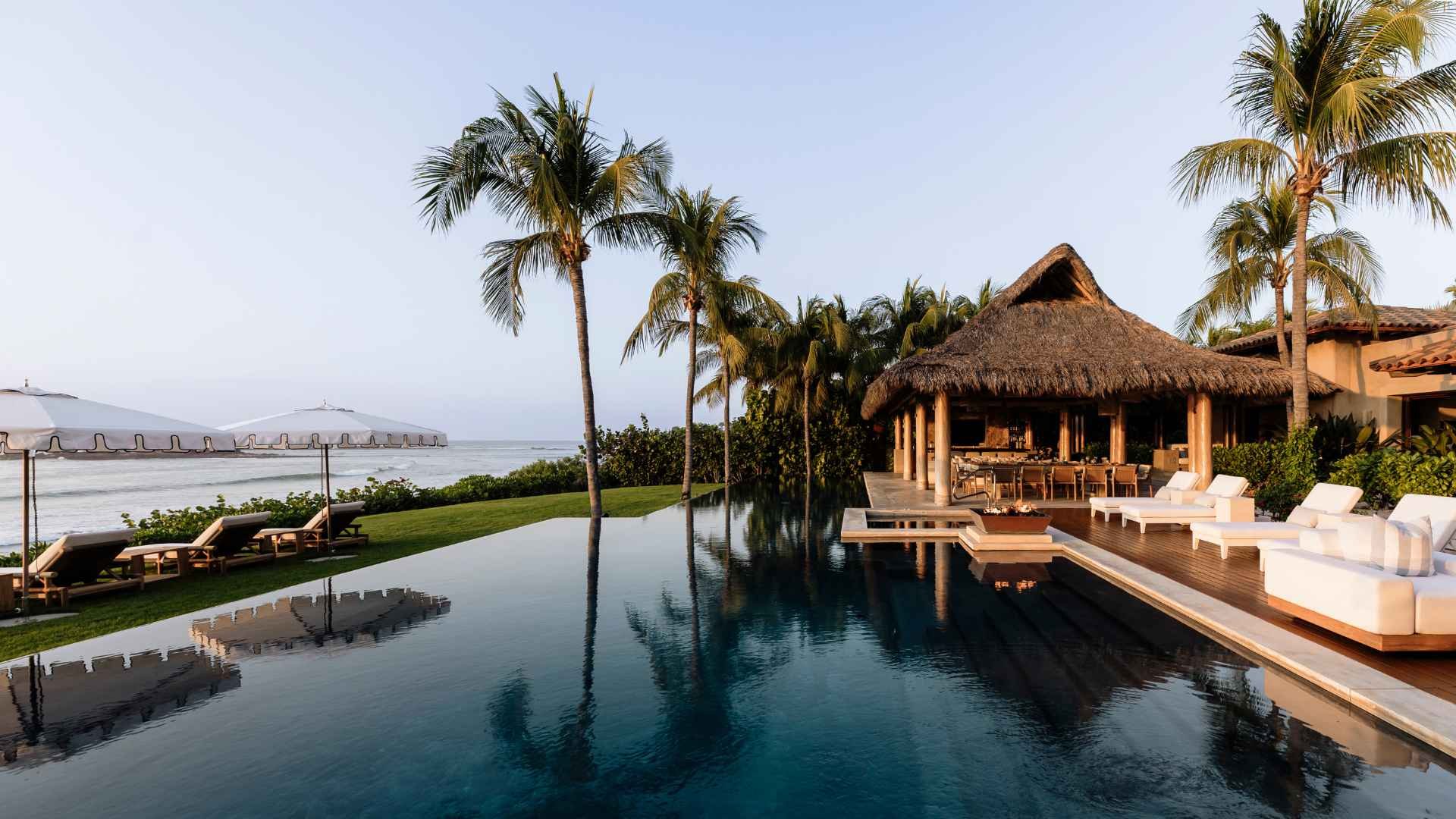 A beachfront villa with a pool and palms.