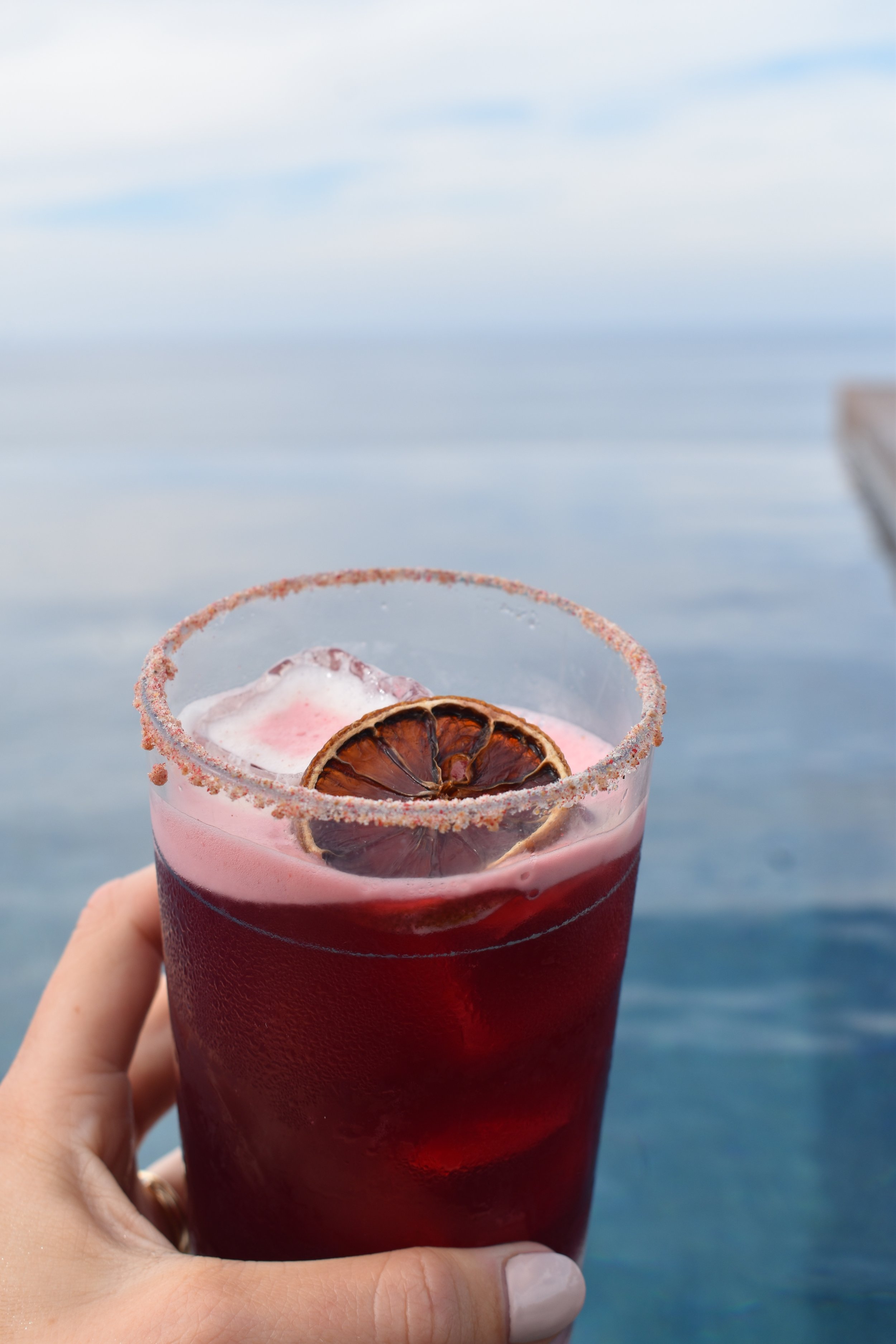 A hand holding a glass of pink wine in the sun.