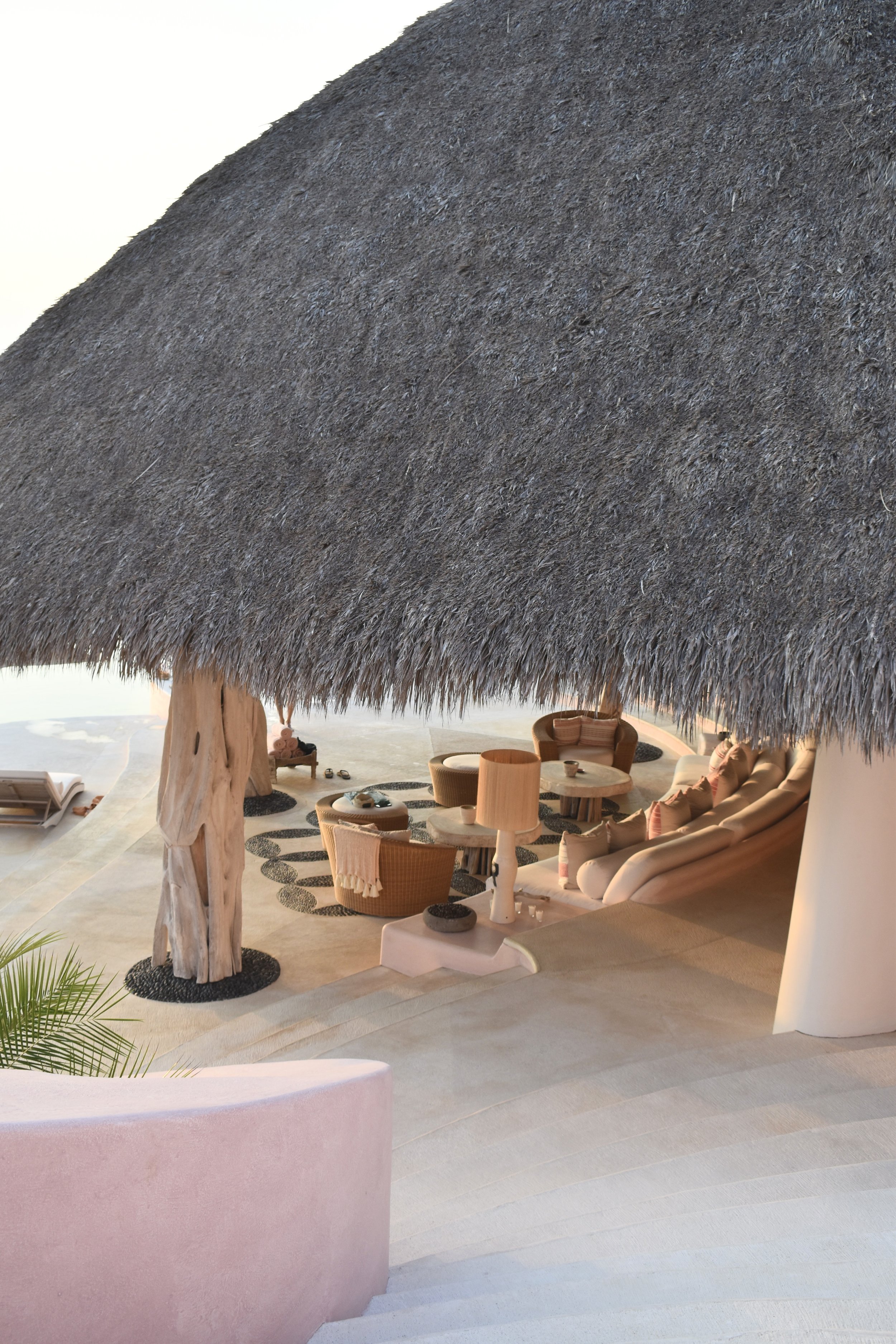 A thatched roof over a lounge area with ocean beyond.