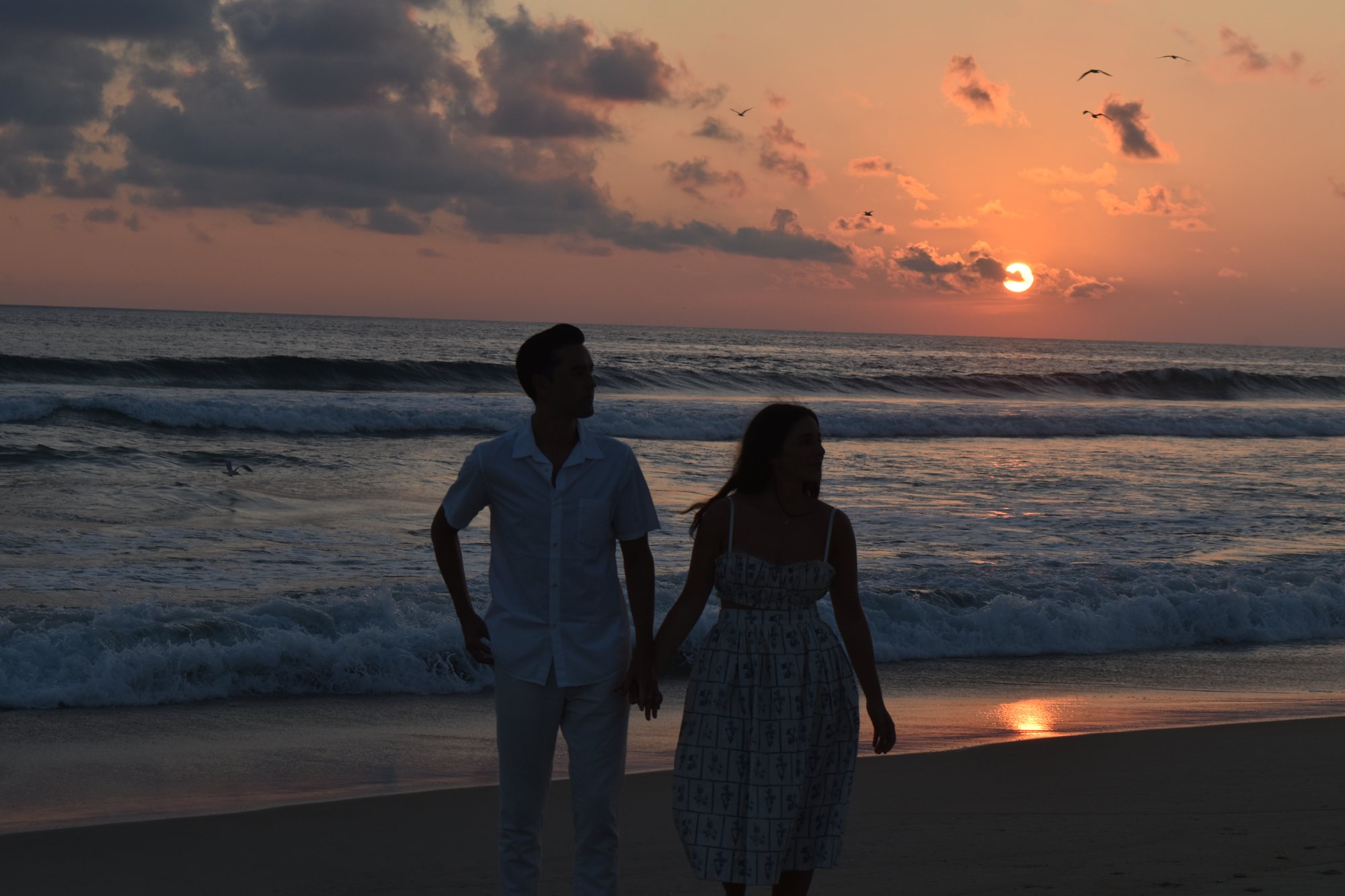 A couple walking a beach at sunset.