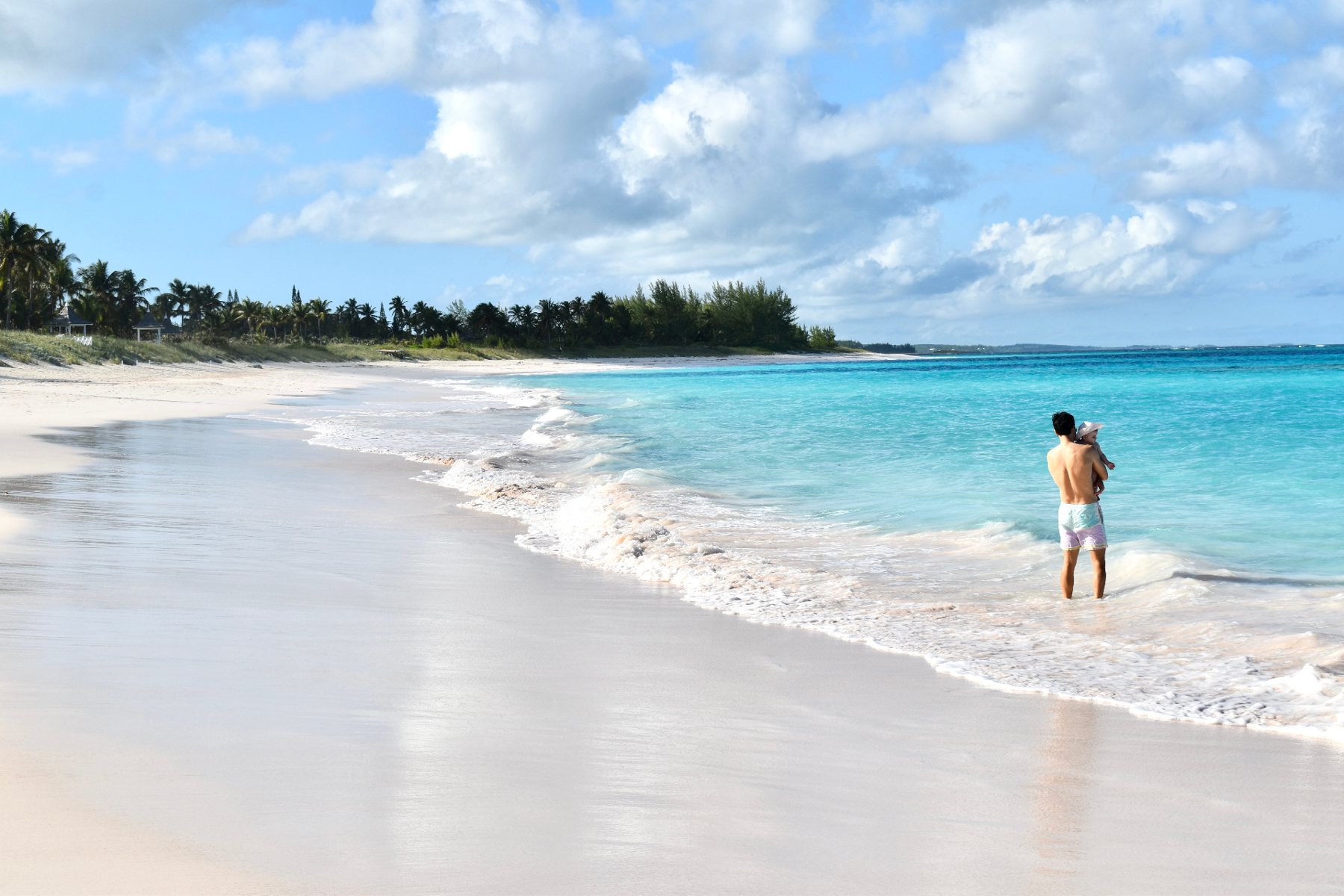 A father holding a child on a turquoise beach.