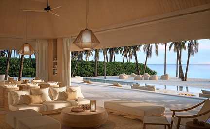 An open-air lounge under a thatched roof by the water.