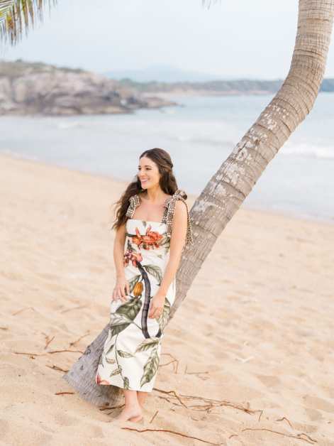 Julia standing beneath a palm tree on the beach.