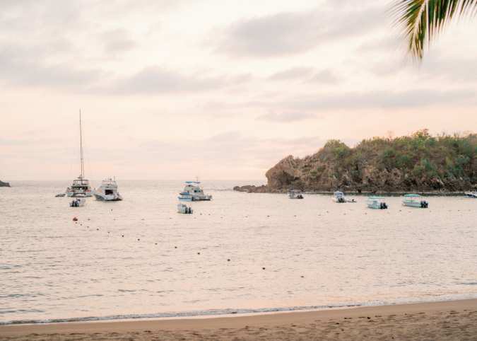 Boats floating on calm pink-hued water at dusk.